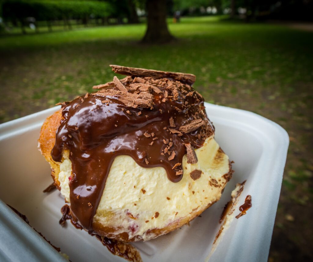 beignet dripping in chocolate in a takeaway tub in a park.