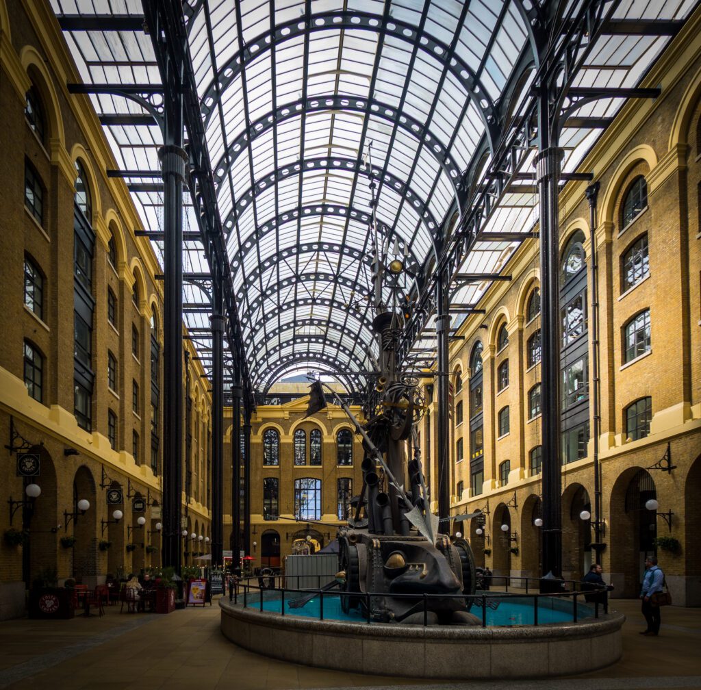 An enormous glass roof covering a converted warehouse with a ship sculpture in the middle