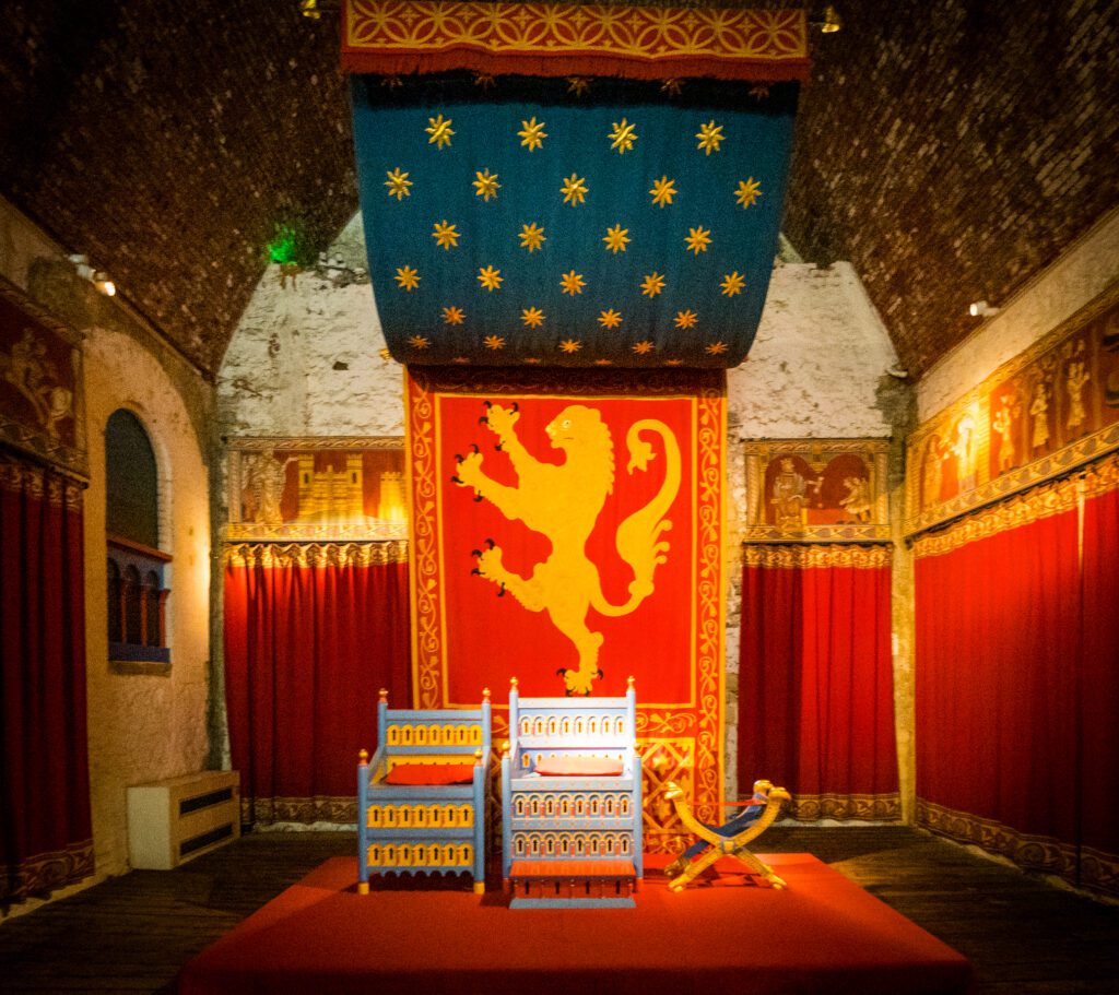 A bright, colourful fabric draped above two wooden thrones