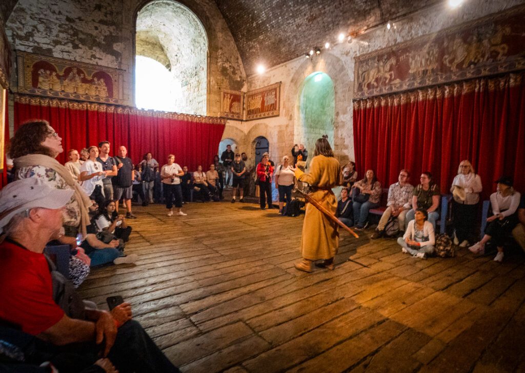 A tour guide, dressed in costume giving a talk to people inside the throne room at Dover Castle