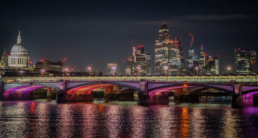 Blackfriars Bridge lit up at night with St. Paul's Cathedral behind and skyscrapers to the right
